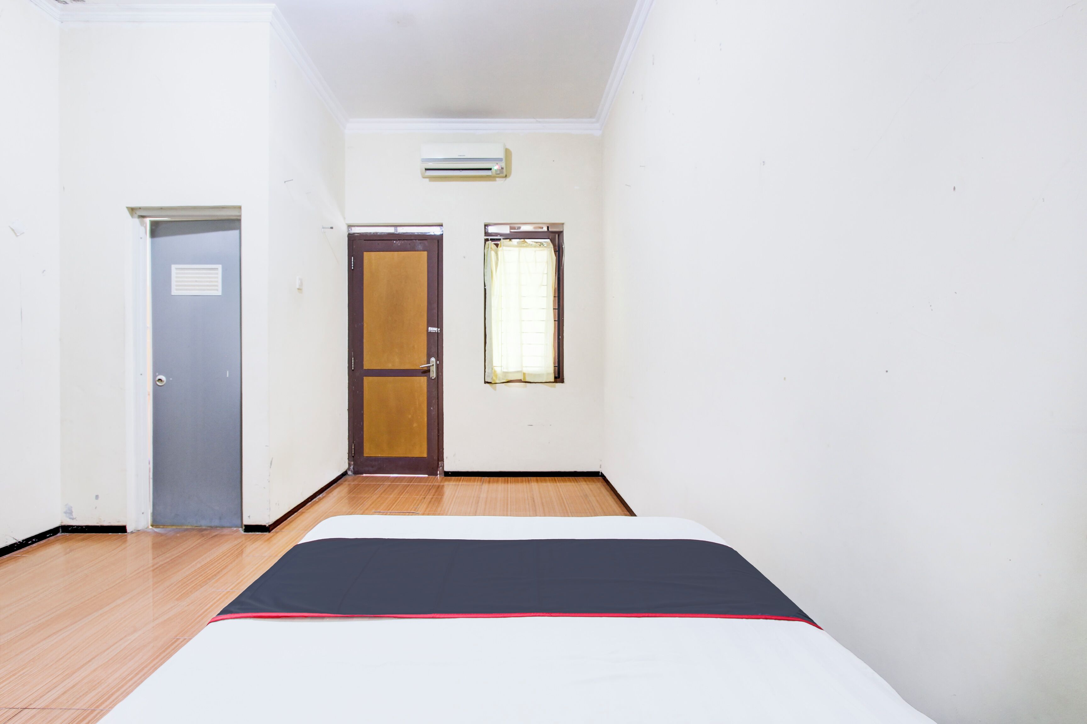 A narrow room with a bed, a door, and a window.