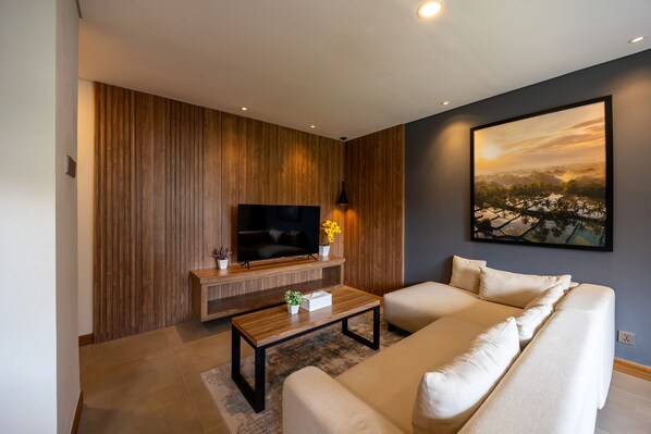 A modern living room with a flat-screen TV, a wooden accent wall, a large painting, and a beige sofa.