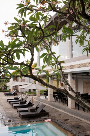 A poolside area with lounge chairs and umbrellas, surrounded by lush greenery and architectural details.
