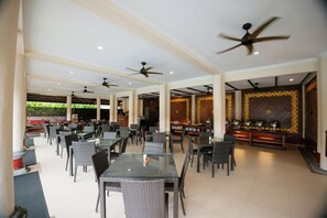 A spacious outdoor dining area with multiple tables and chairs, ceiling fans, and a decorative wall with a geometric pattern. - Kana Suites Nusa Dua By Fays Hospitality (Nusa Dua)