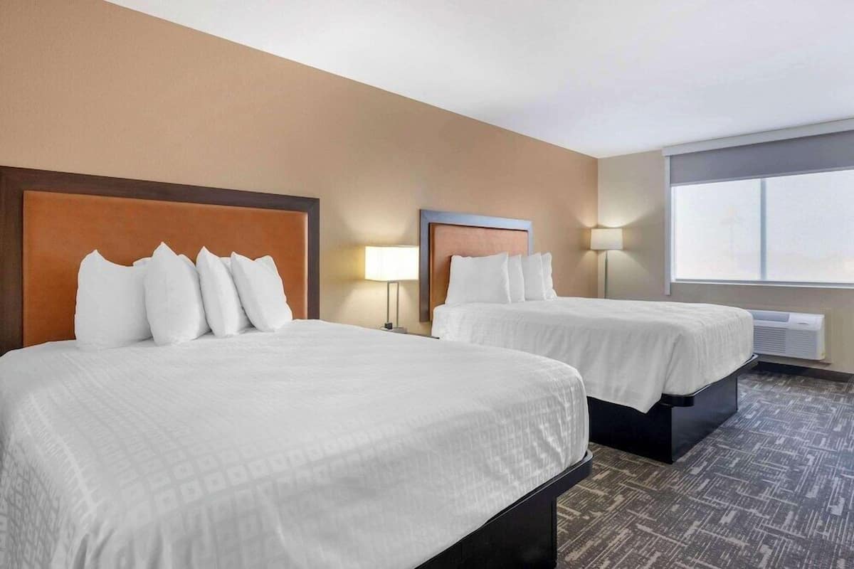 A hotel room with two beds, a large window, and a wall-mounted air conditioner.