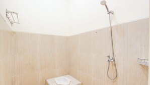 Ett litet, kaklat duschutrymme med ett duschmunstycke som kan hållas i handen och en liten pall.