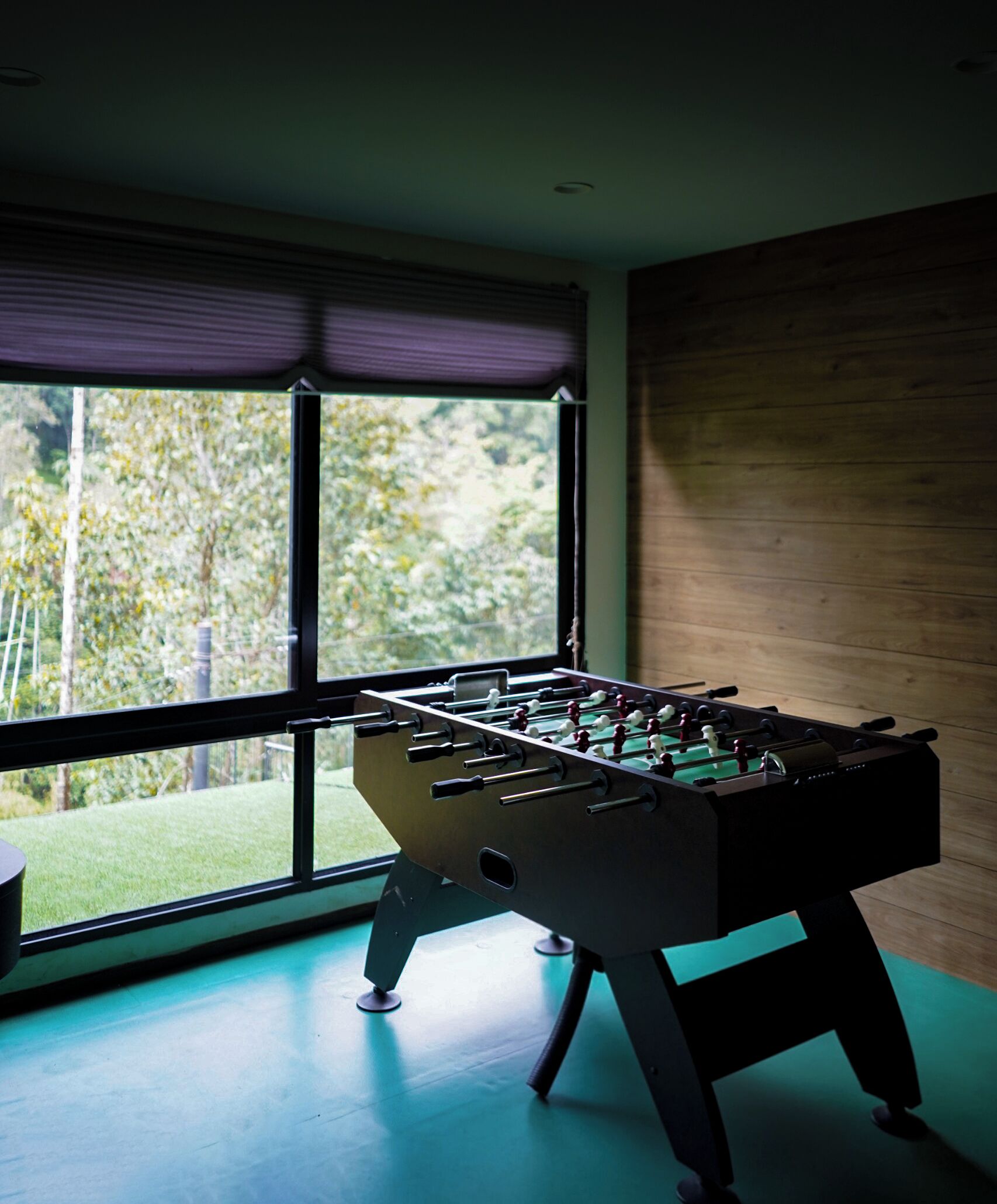 A foosball table in a room with large windows, a wooden wall, and a blue floor.