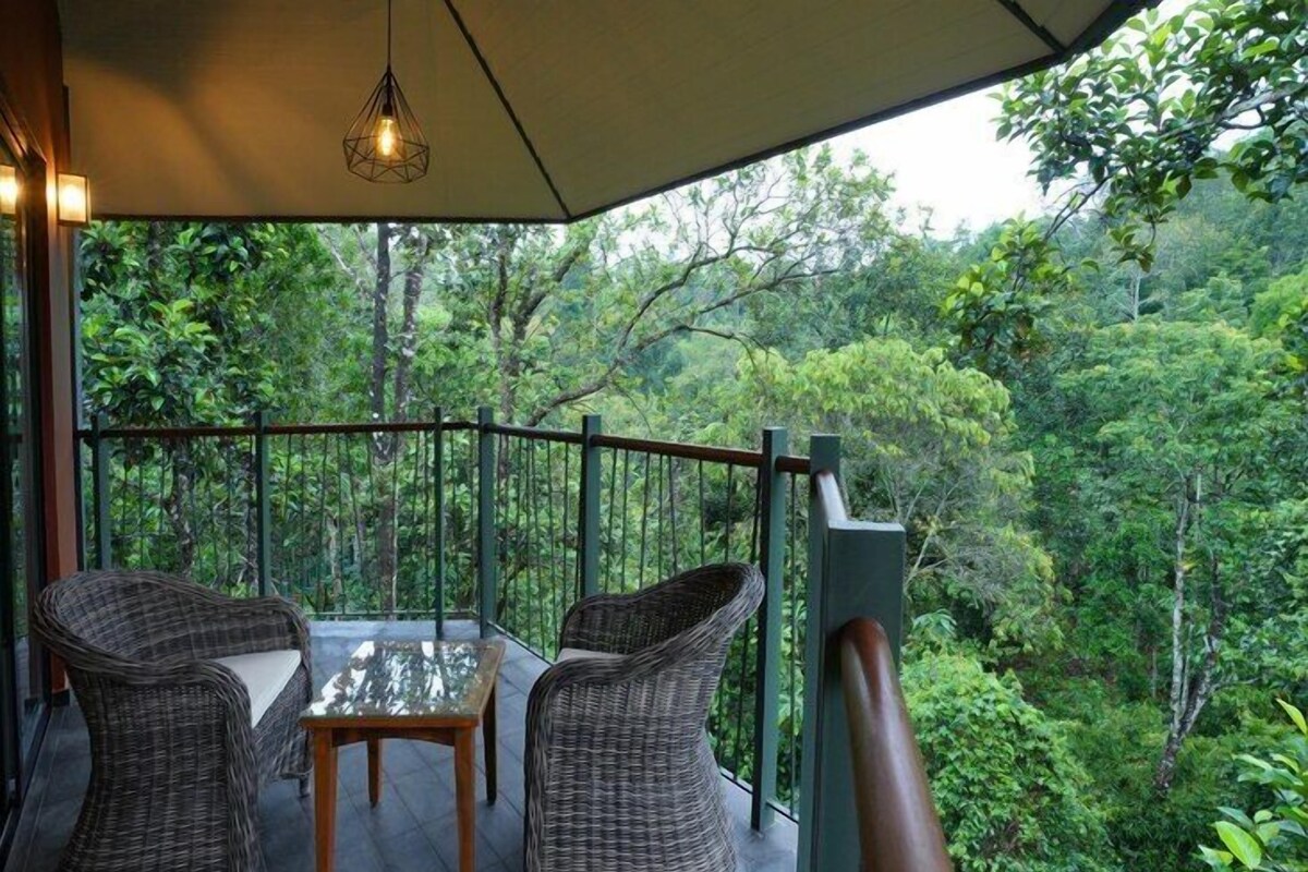 Un balcon agrémenté de meubles en osier et d’une table en verre, offrant une vue sur une forêt luxuriante.
