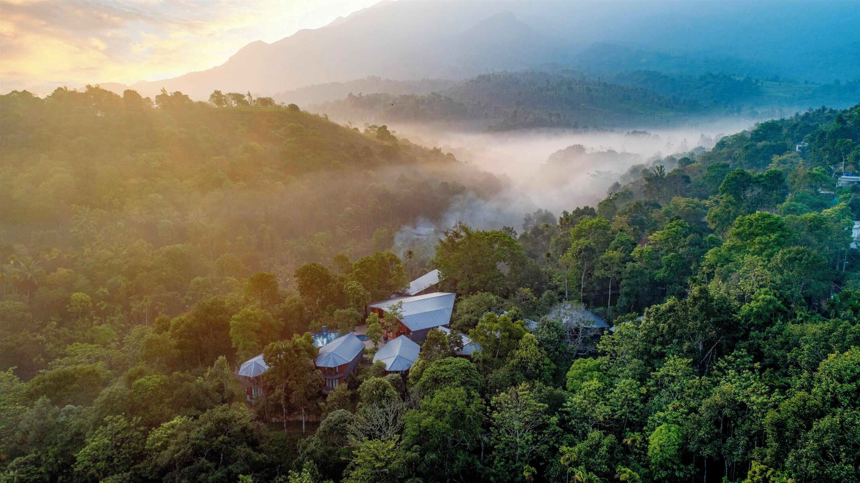 A mountainous landscape with a valley, houses with blue roofs, and dense greenery.