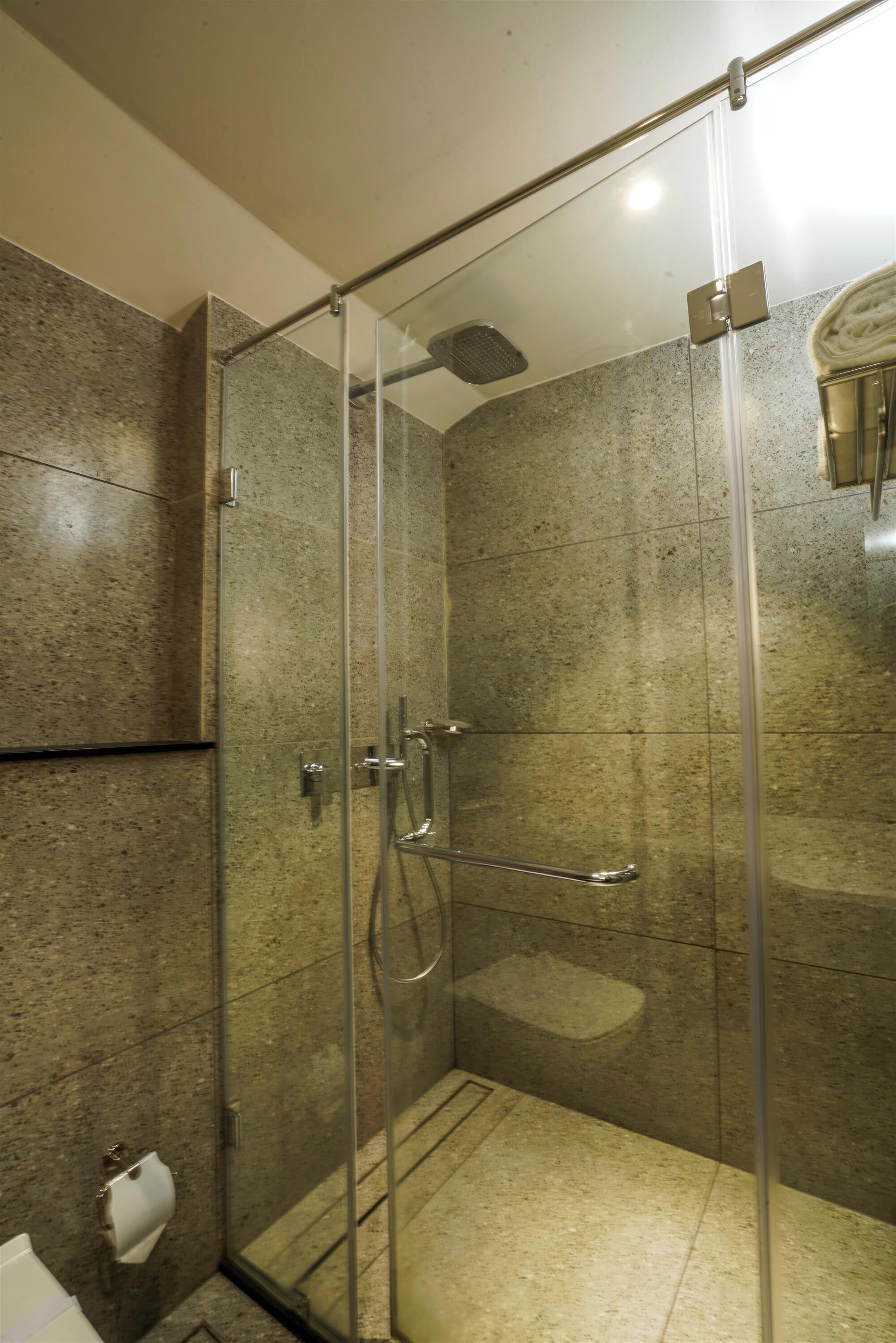 Cabina de ducha con paredes de vidrio, un cabezal de ducha manual y un grifo instalado en la pared.