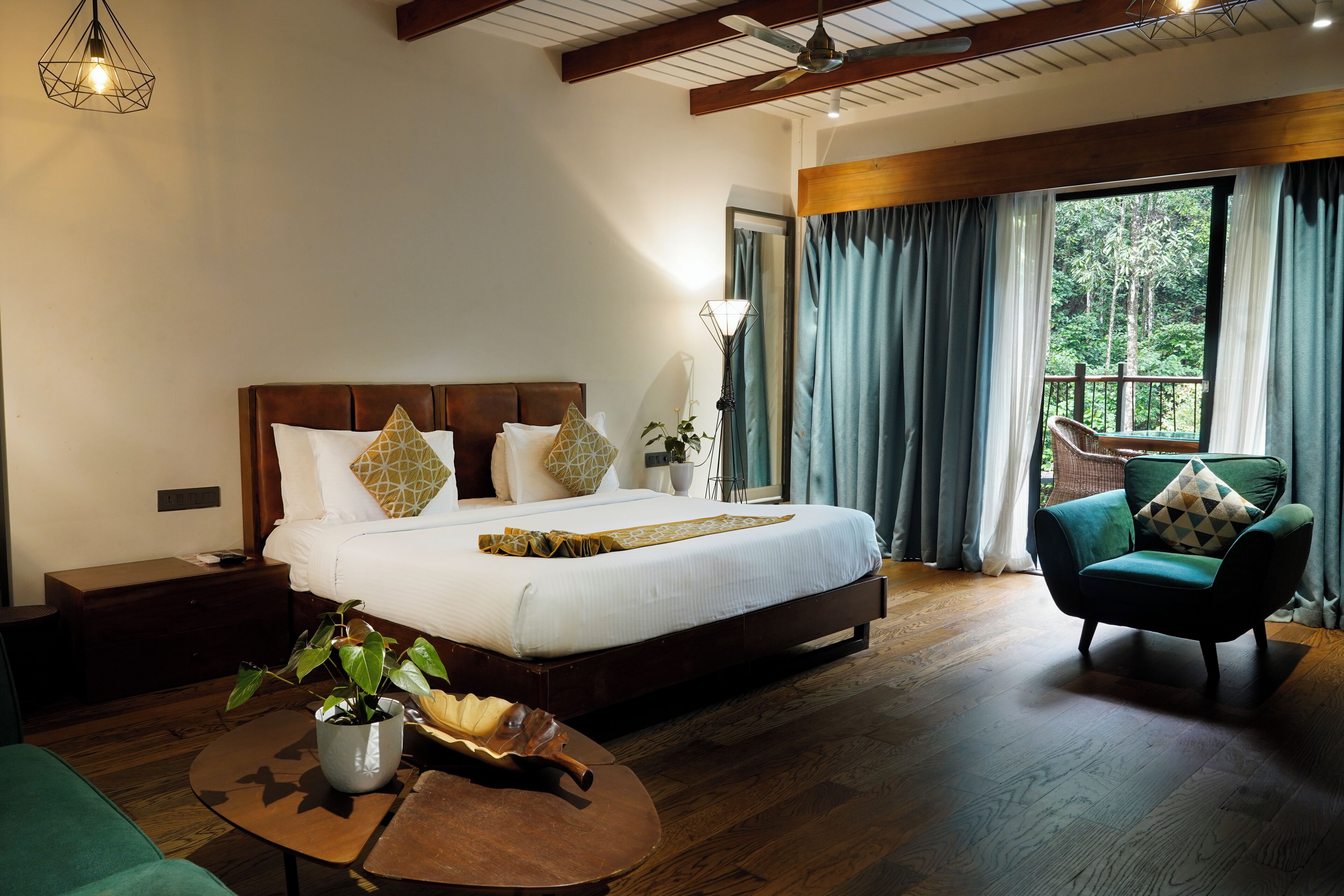 Un dormitorio espacioso con una cama grande, suelo de madera, un sillón verde y vistas al exterior a través de una ventana.