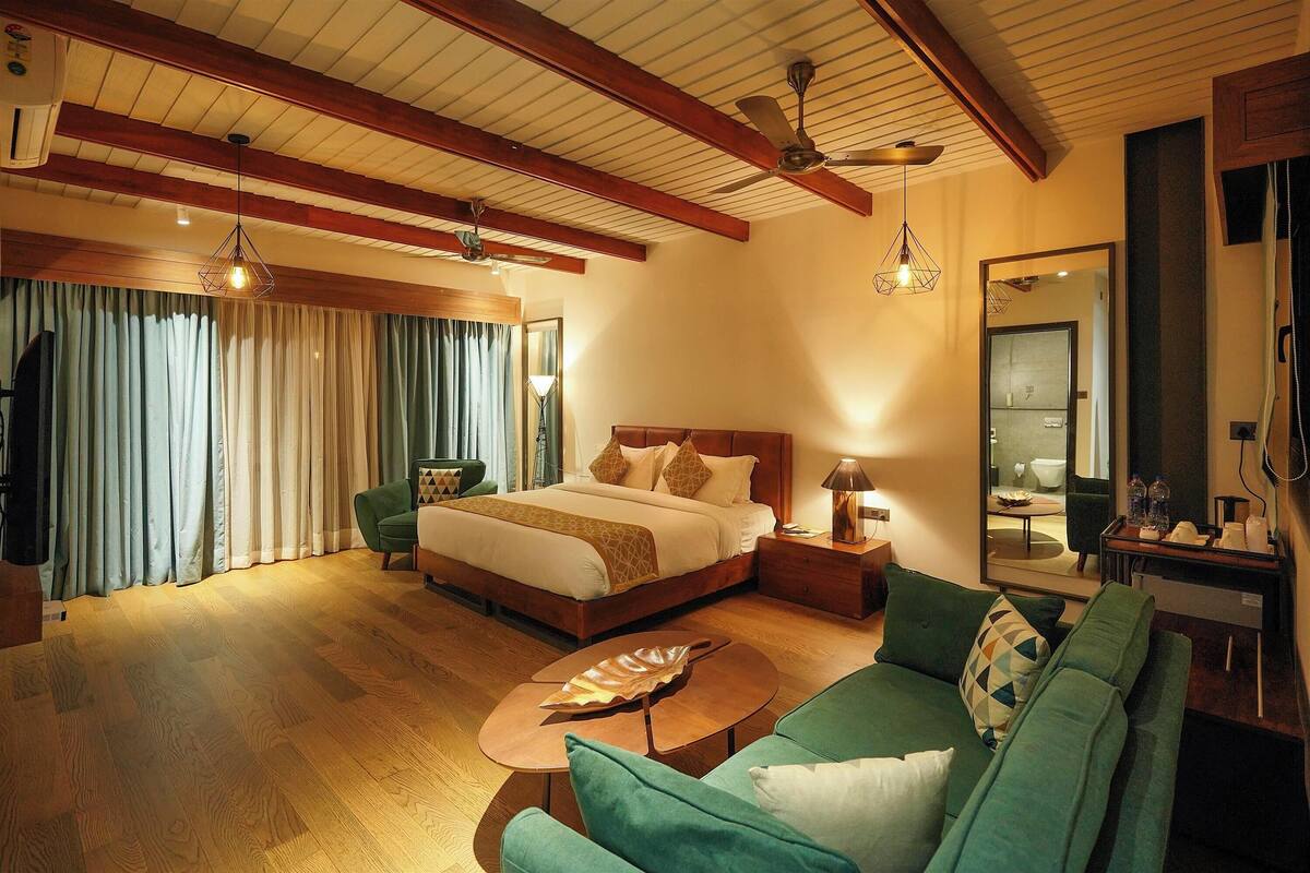 A hotel room with a large bed, a green sofa, a wooden coffee table, and a ceiling fan.