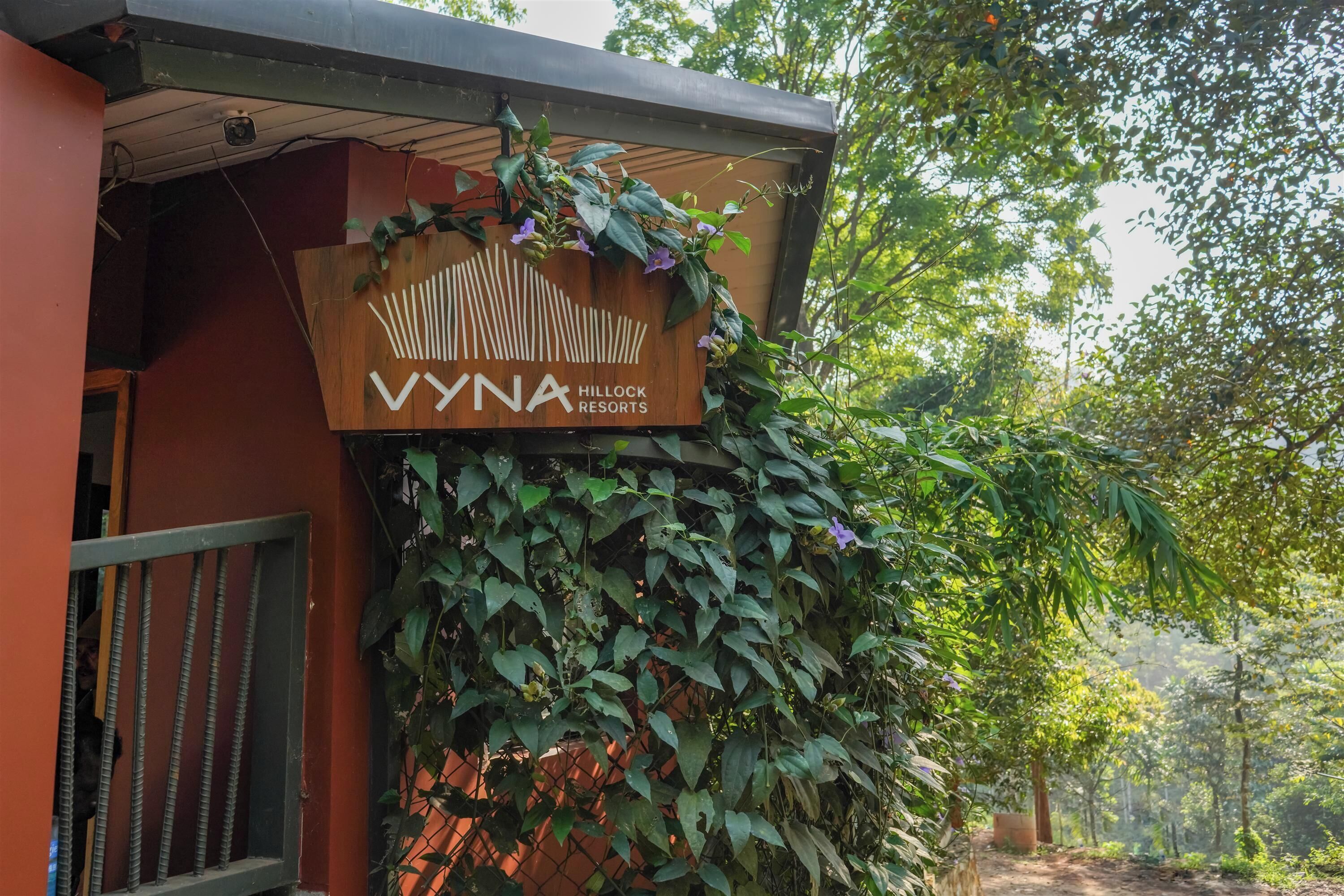 Señal de VYNA Hillock Resorts con estructura de madera y plantas trepadoras.