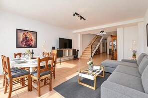 Un'ampia zona giorno con tavolo da pranzo per quattro persone, un divano grigio, una scala e una televisione a schermo piatto.