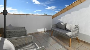 Una terrazza sul tetto con un muro bianco, un divano grigio e poltrone in vimini.