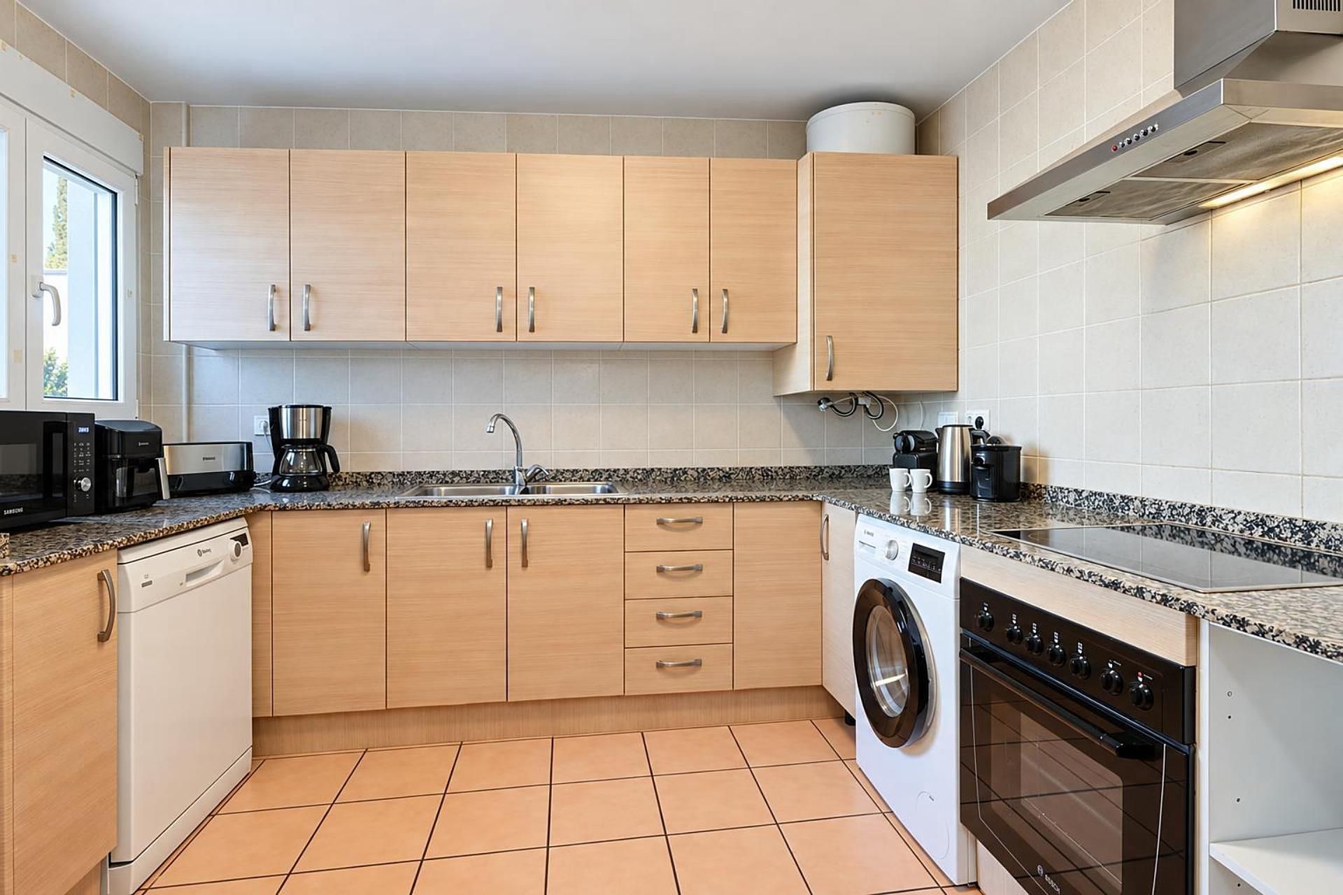 A modern kitchen with wooden cabinets, a built-in dishwasher, a washing machine, and a stove.