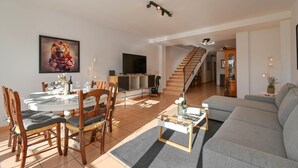 Un soggiorno moderno con zona pranzo, una scala e un televisore a schermo piatto.
