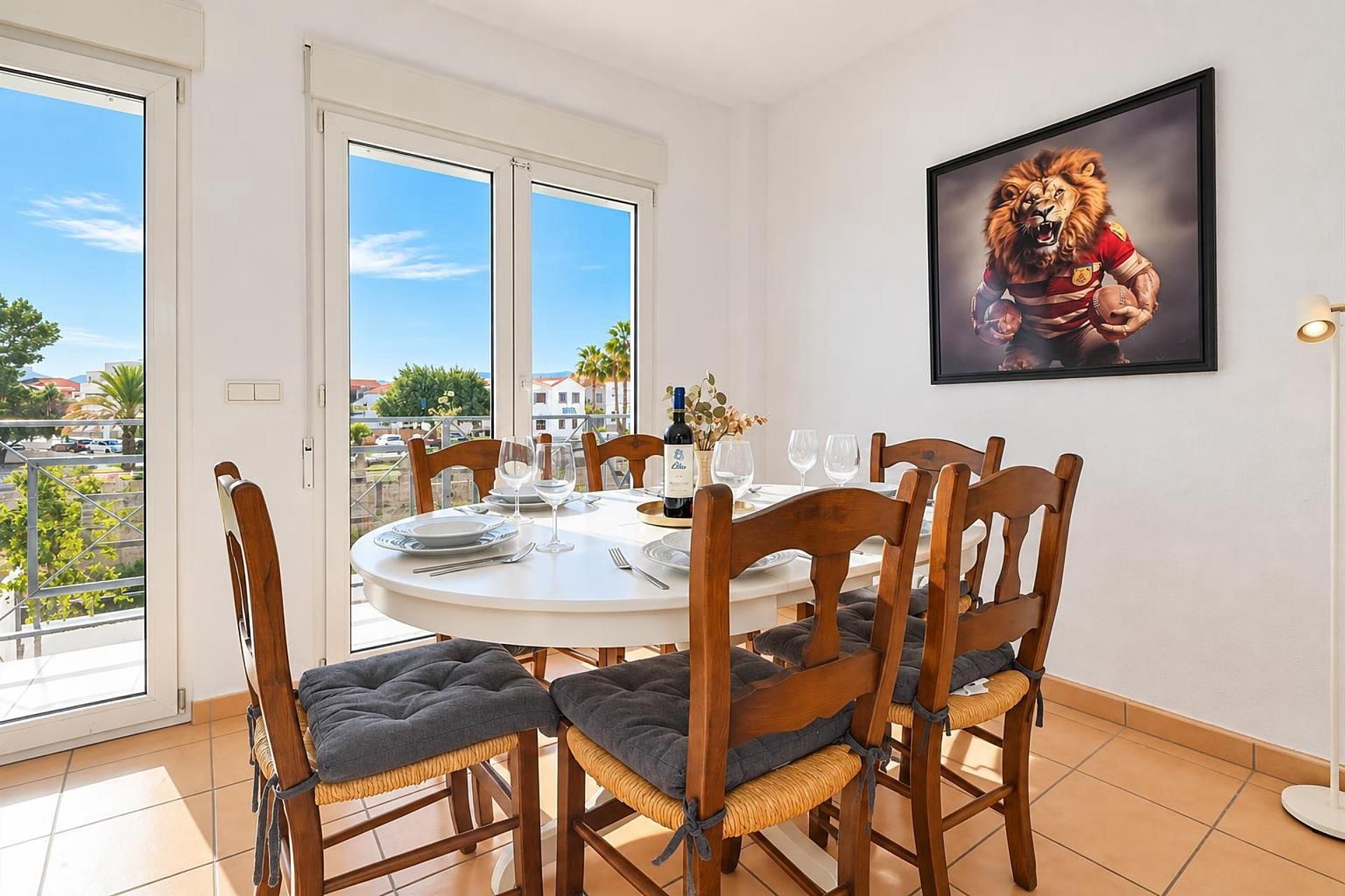 A dining area with a round table, chairs, and a view through large windows.