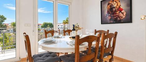 A dining area with a round table, chairs, and a view through large windows.