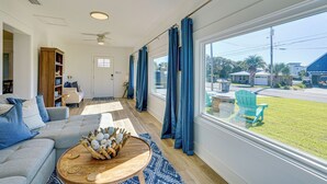 A spacious living room with a large window, a ceiling fan, a wooden coffee table, and a blue chair outside. - Walk to Beach: Chic PCB Getaway w/ Yard (Panama City Beach)