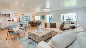 A spacious living area with a large sofa, a coffee table, and a dining area in the background. - Walk to Beach: Chic PCB Getaway w/ Yard (Panama City Beach)