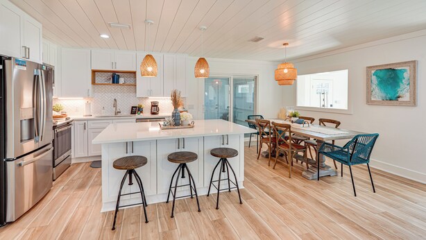 A modern kitchen with white cabinets, a large island with stools, stainless steel appliances, and pendant lighting. - Walk to Beach: Chic PCB Getaway w/ Yard (Panama City Beach)