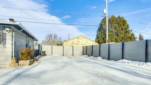 Ein verschneiter Weg führt zu einem Haus mit Garage, Holzzaun und Baum im Hintergrund.