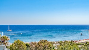 Vista costeira com um veleiro, guarda-sóis de praia e um céu azul límpido.