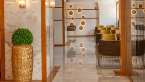 Um hall de hotel moderno com piso de mármore, balcão de recepção e área de estar com cadeiras.