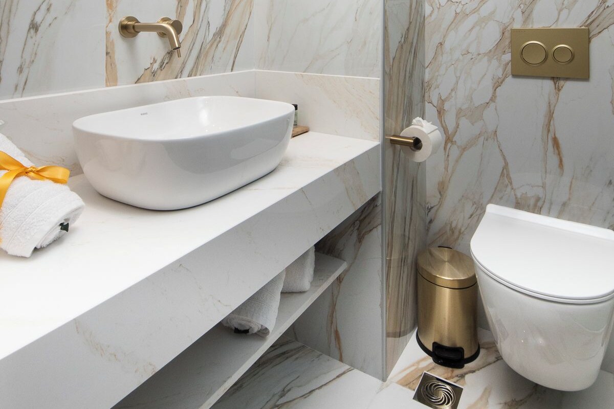 A modern bathroom with a white marble vanity, a gold-framed mirror, and a toilet with a gold bidet attachment.