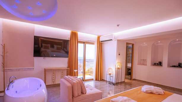 Quarto de hotel moderno com uma banheira grande, um sofá, uma cama e vista para o exterior.