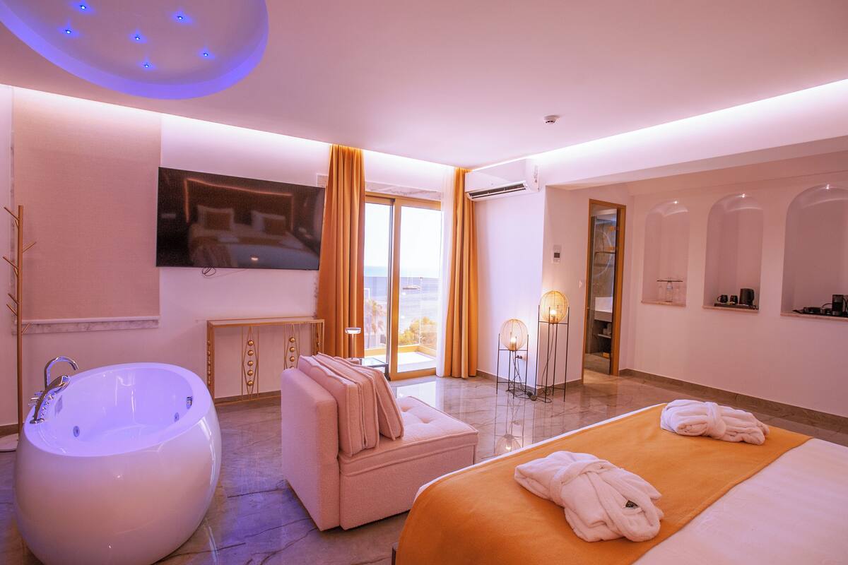 Habitación de hotel moderna con una bañera grande, un sofá, una cama y vistas al exterior.