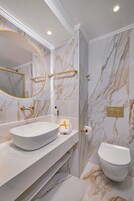 Un baño con tocador de mármol, espejo redondo, inodoro y perchero.
