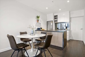 A modern kitchen with white cabinets, a central island, and a dining area with a round table and four chairs.