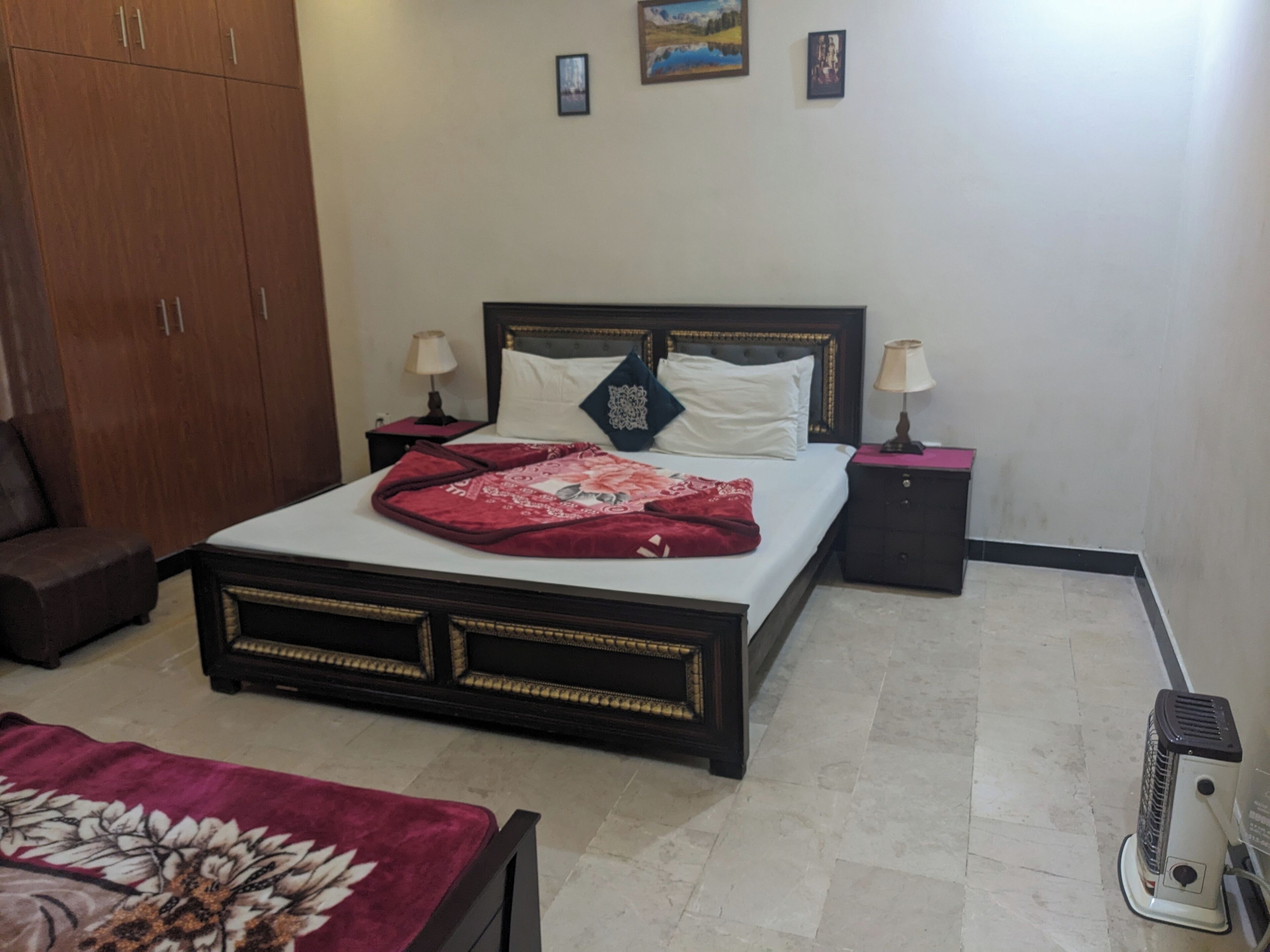 A neatly arranged bedroom with a bed, two bedside tables, a nightstand, a wardrobe, and a heater.