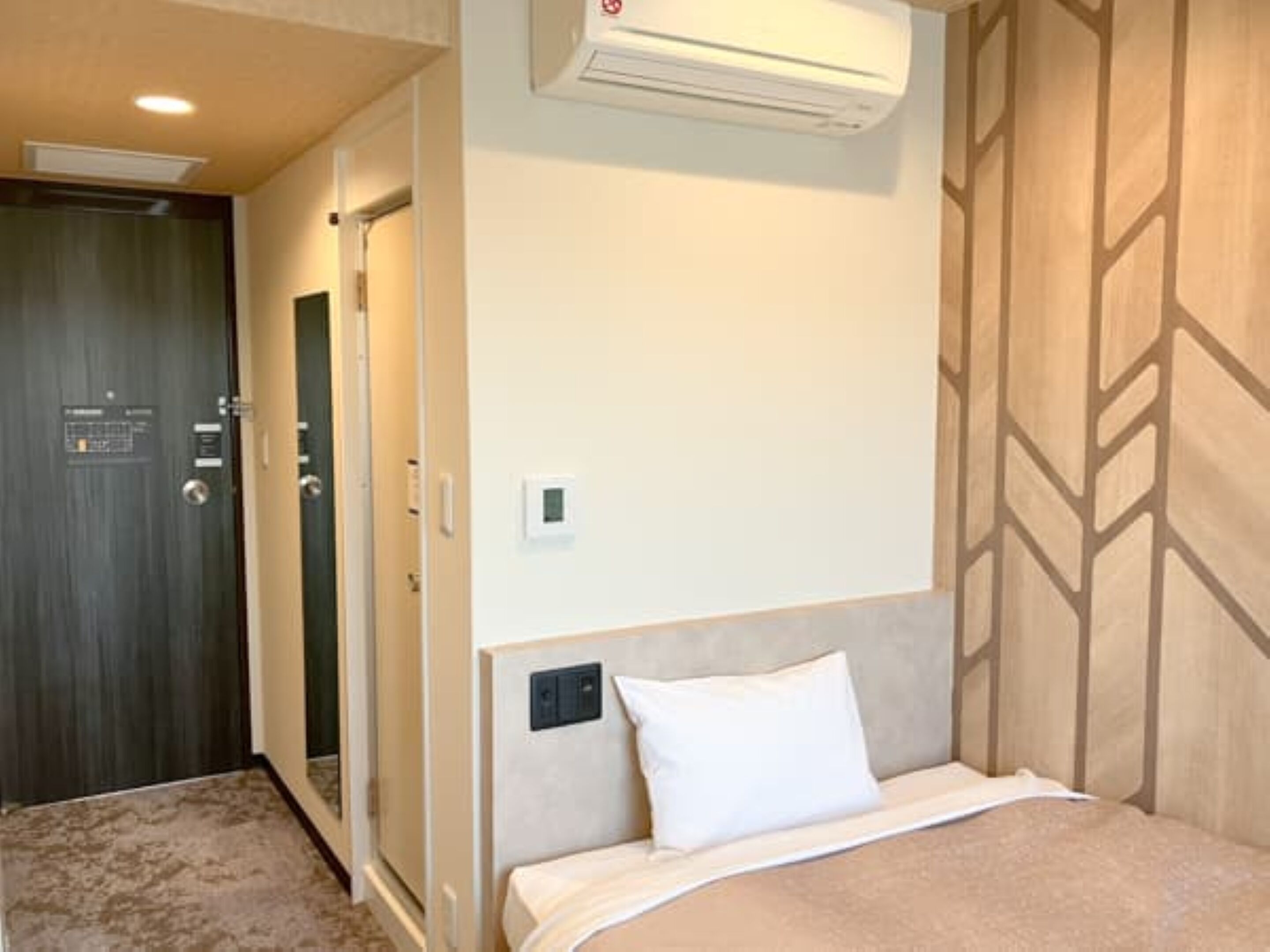 Een hotelkamer met een bed, een wandairconditioner, een deur en een behang met patroon.