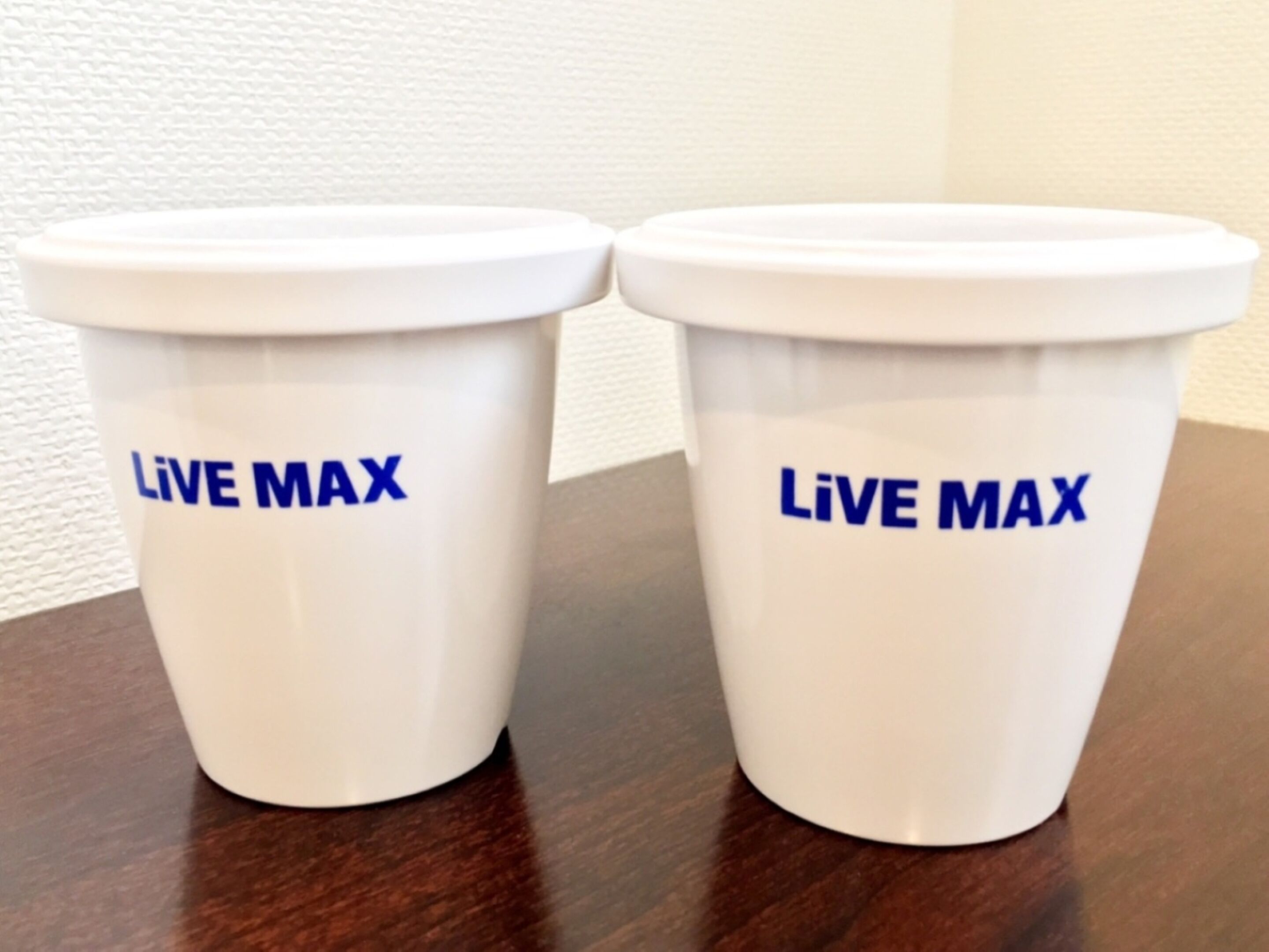 Two white disposable cups with blue text on a wooden table.