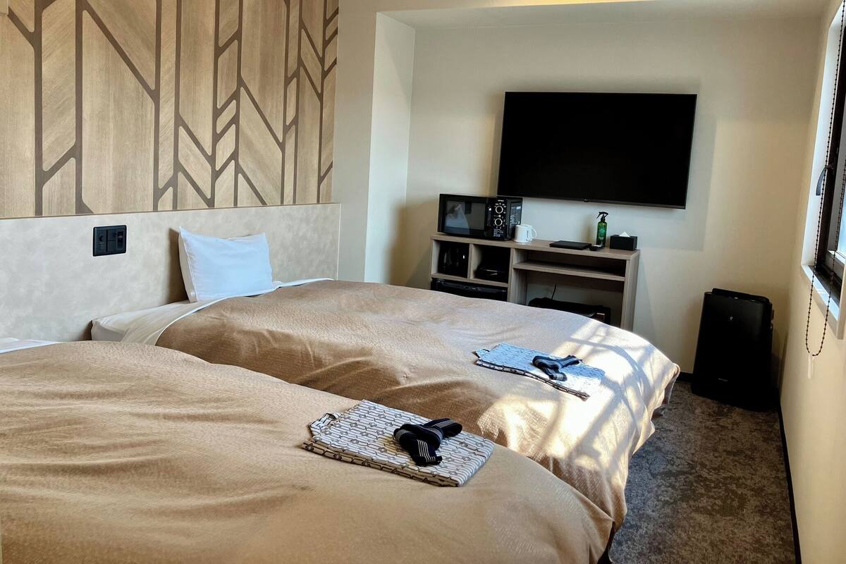 Ein Hotelzimmer mit zwei Betten, einem Fernseher, einer Mikrowelle, einer Kaffeemaschine und einem kleinen Tisch mit Notizbuch und Stift.