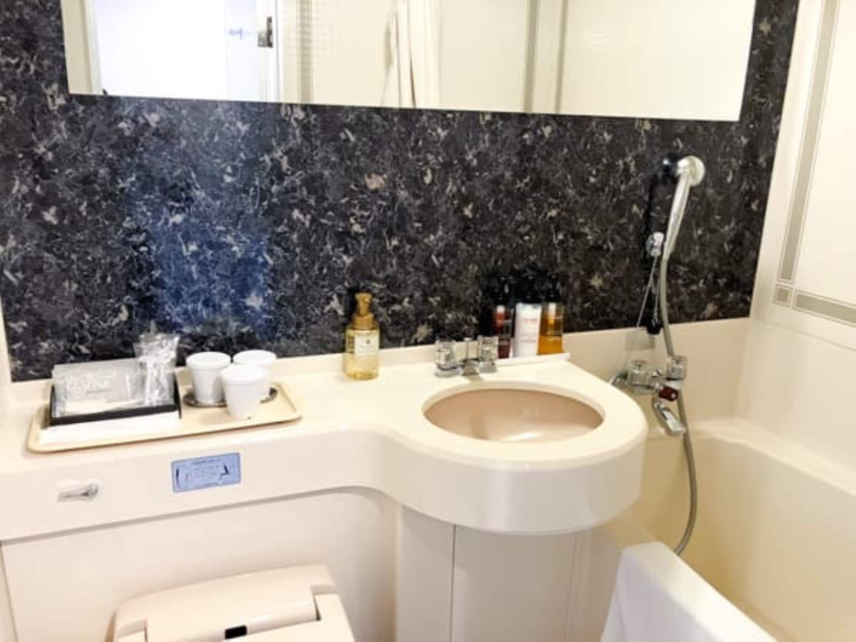 Ein Badezimmer mit Marmorfliesenwand, einem Waschbecken, einem Spiegel und einer Dusche.