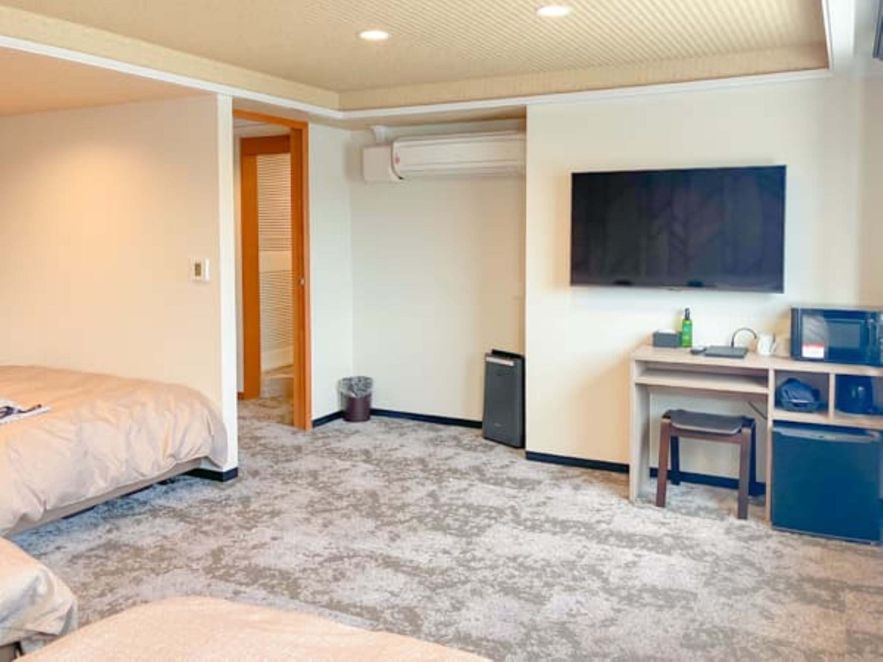 A bedroom with a bed, a desk, a chair, a TV, and a trash can.