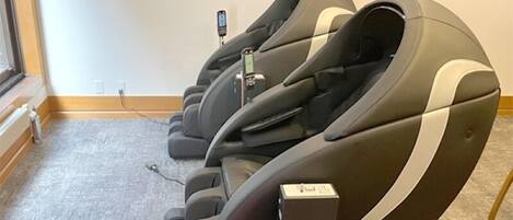 Une rangée de fauteuils de massage dans une pièce dont le sol est recouvert d’une moquette et où un téléviseur est fixé au mur.