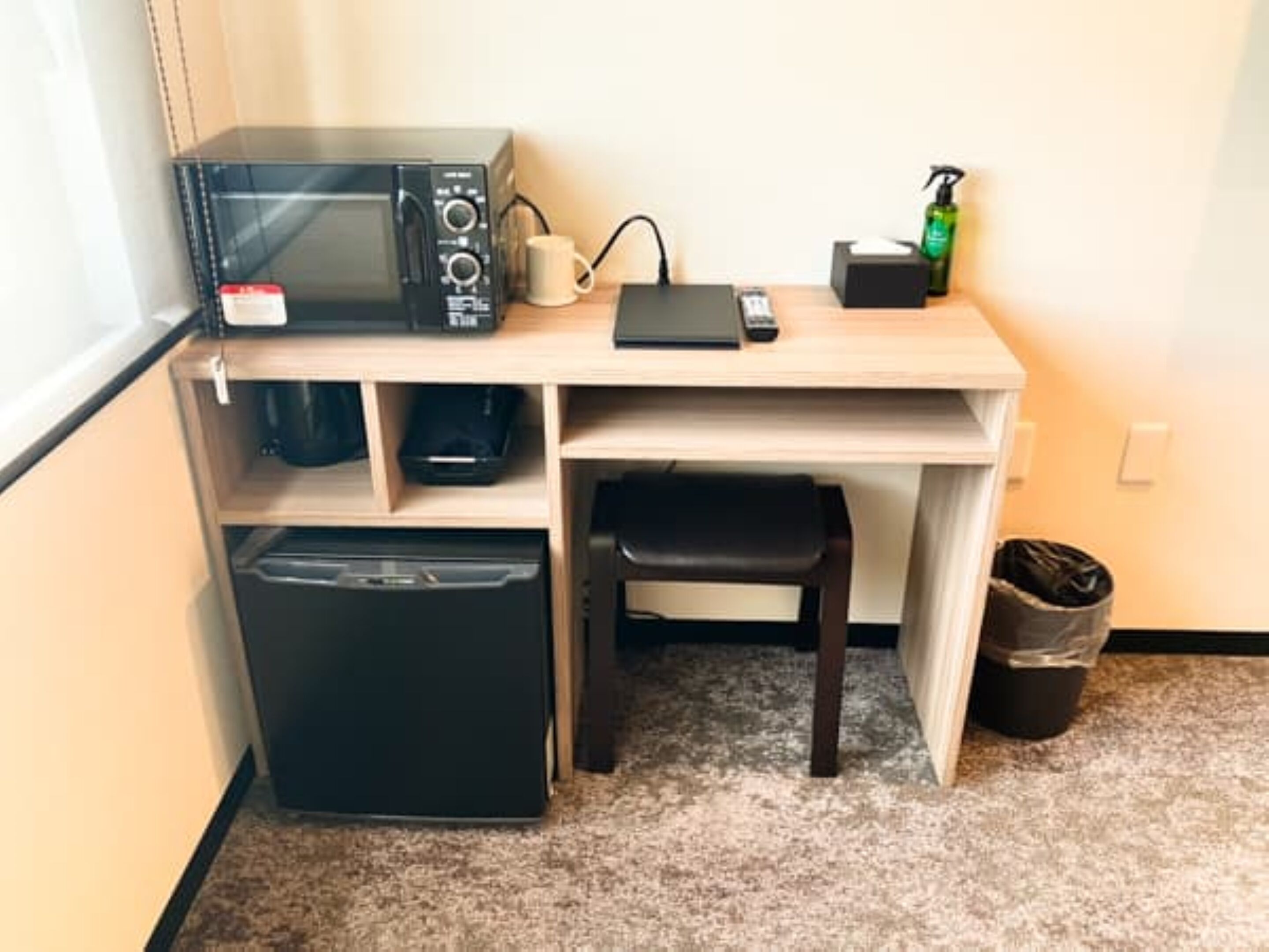 A compact kitchenette with a microwave, coffee maker, and a trash bin.