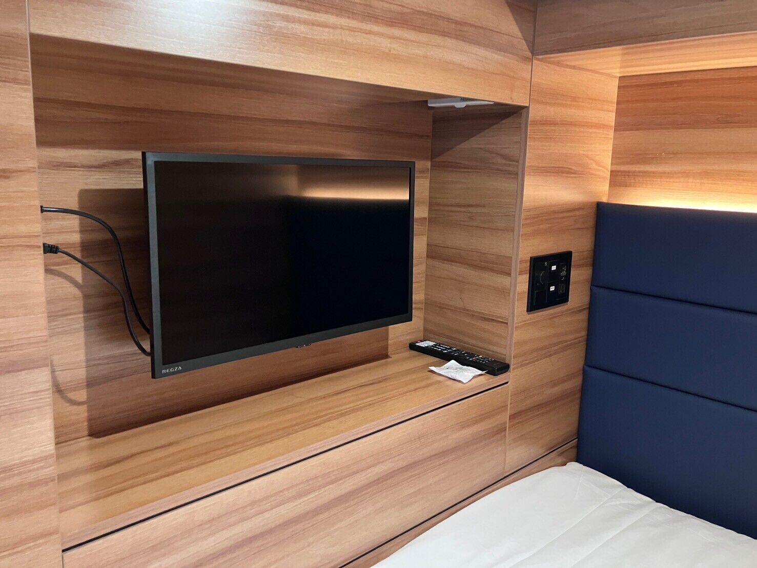 A modern room with a mounted flat-screen TV, a remote control, and a power outlet on the wall.