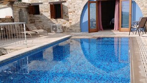 Une piscine aux carreaux de mosaïque, un bâtiment en pierre doté d’une arche bleue et des espaces de détente en plein air.