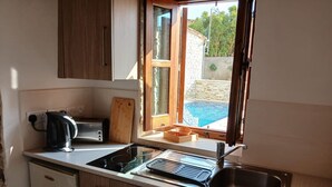 Une cuisine compacte avec une fenêtre, un grille-pain, une bouilloire, un évier et une planche à découper en bois.