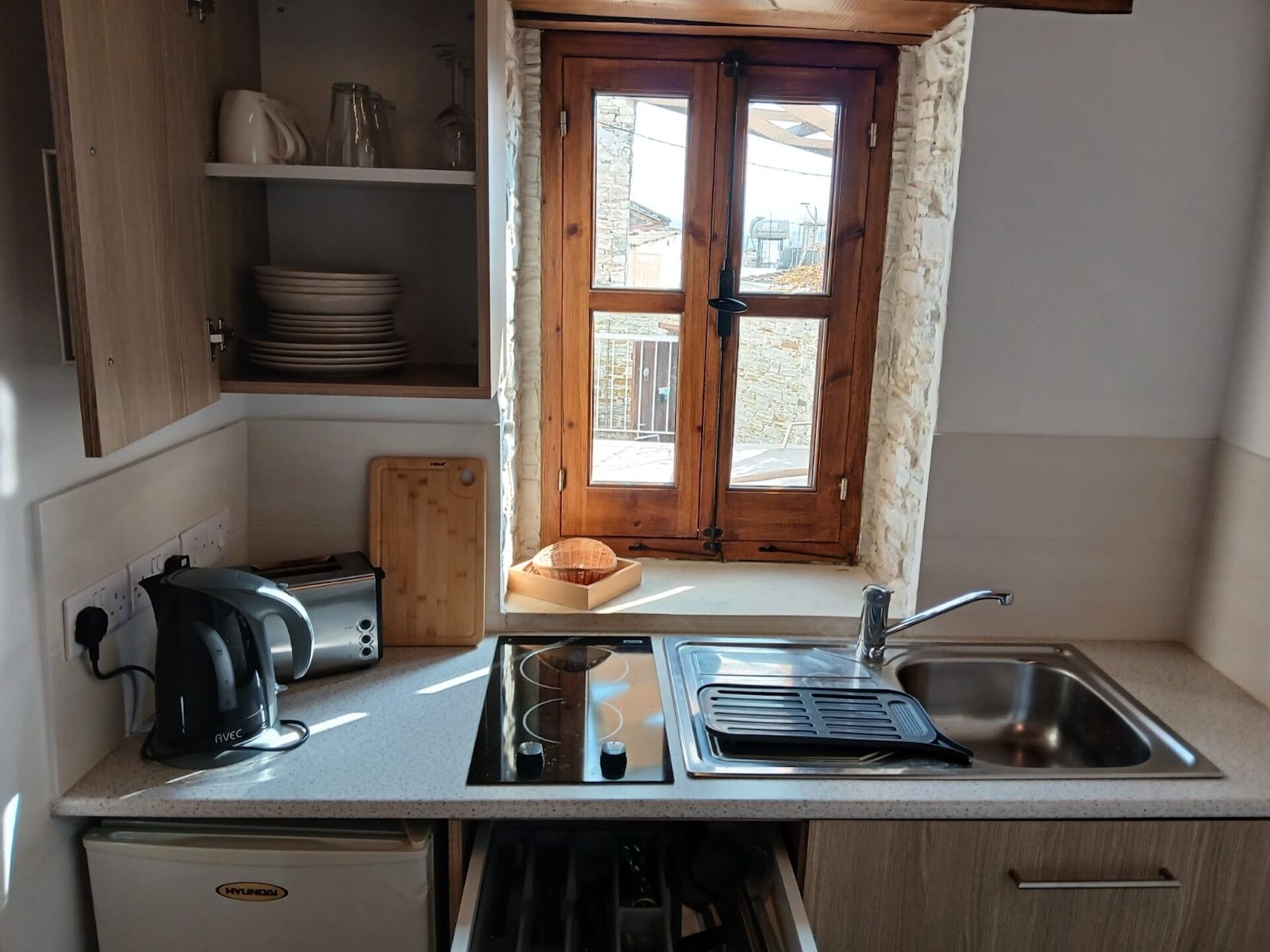 A compact kitchen with a window, a kettle, a toaster, a sink, and a dishwasher.