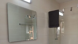 Une salle de bain avec un lavabo blanc, un miroir, une douchette à main et un porte-serviettes.