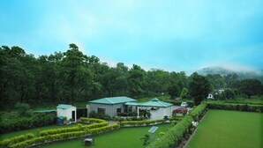 A lush green landscape with a building featuring a green roof, surrounded by manicured hedges and a well-maintained lawn. - Vasant Corbett Resort (Ramnagar)