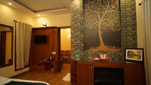 A hotel room with a bed, a wooden cabinet, a fireplace, a TV, and a decorative wall. - Vasant Corbett Resort (Ramnagar)