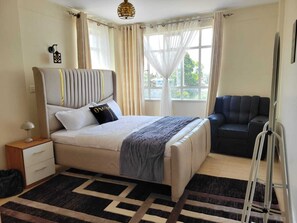 Relax in this serene bedroom with a large bed, bedside table, and sofa, offering a view of lush greenery.