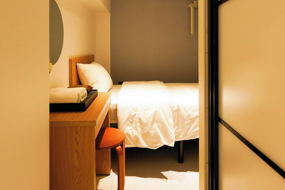 Ein Hotelzimmer mit Bett, Schreibtisch mit Stuhl, einem kleinen Tisch, einem Spiegel und einer Tür.