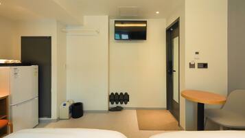 A hotel room with two beds, a refrigerator, a TV mounted on the wall, a small table, and a chair.