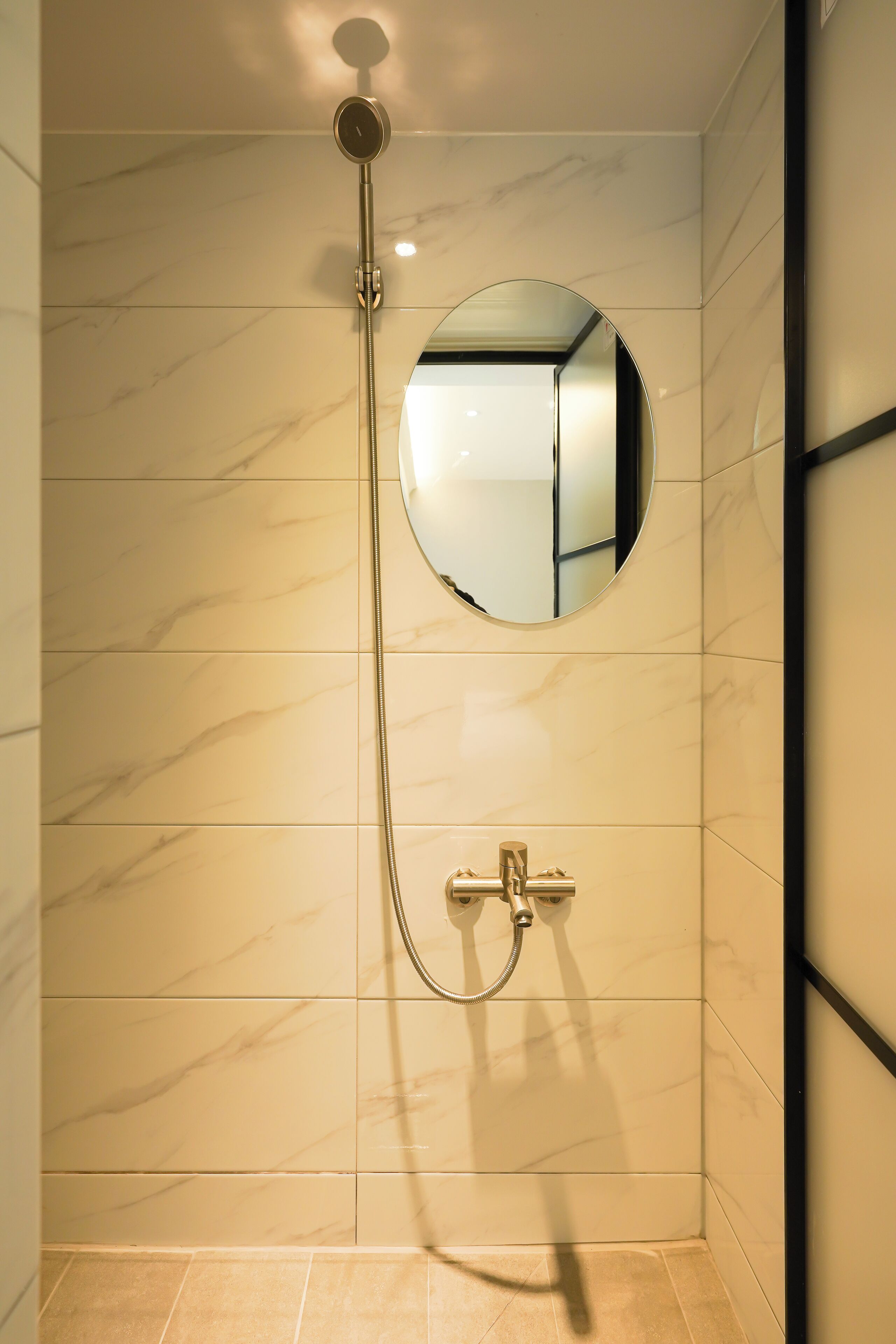 Eine Dusche mit Handbrause und einem spiegelnden Wandspiegel.