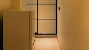 A narrow hallway with a refrigerator on the left, a tiled floor, and a wall with a black frame and a vent. - Han stay (Seoul)